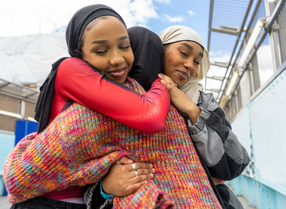 Young women wearing hijabs hugging in city